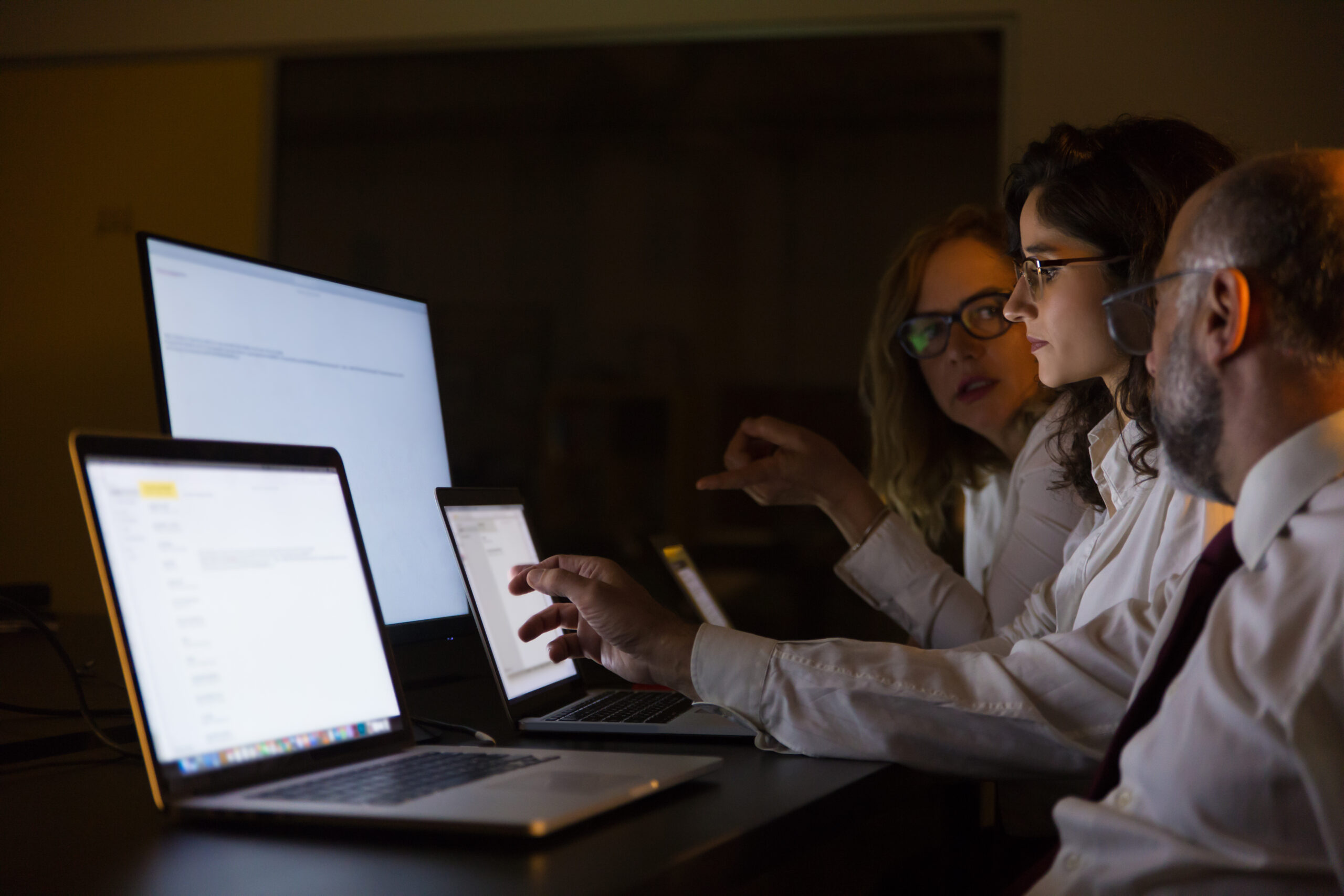 A group of business professionals collaborating on cybersecurity strategies in a dark office, discussing how to empower employees to combat cyber threats.