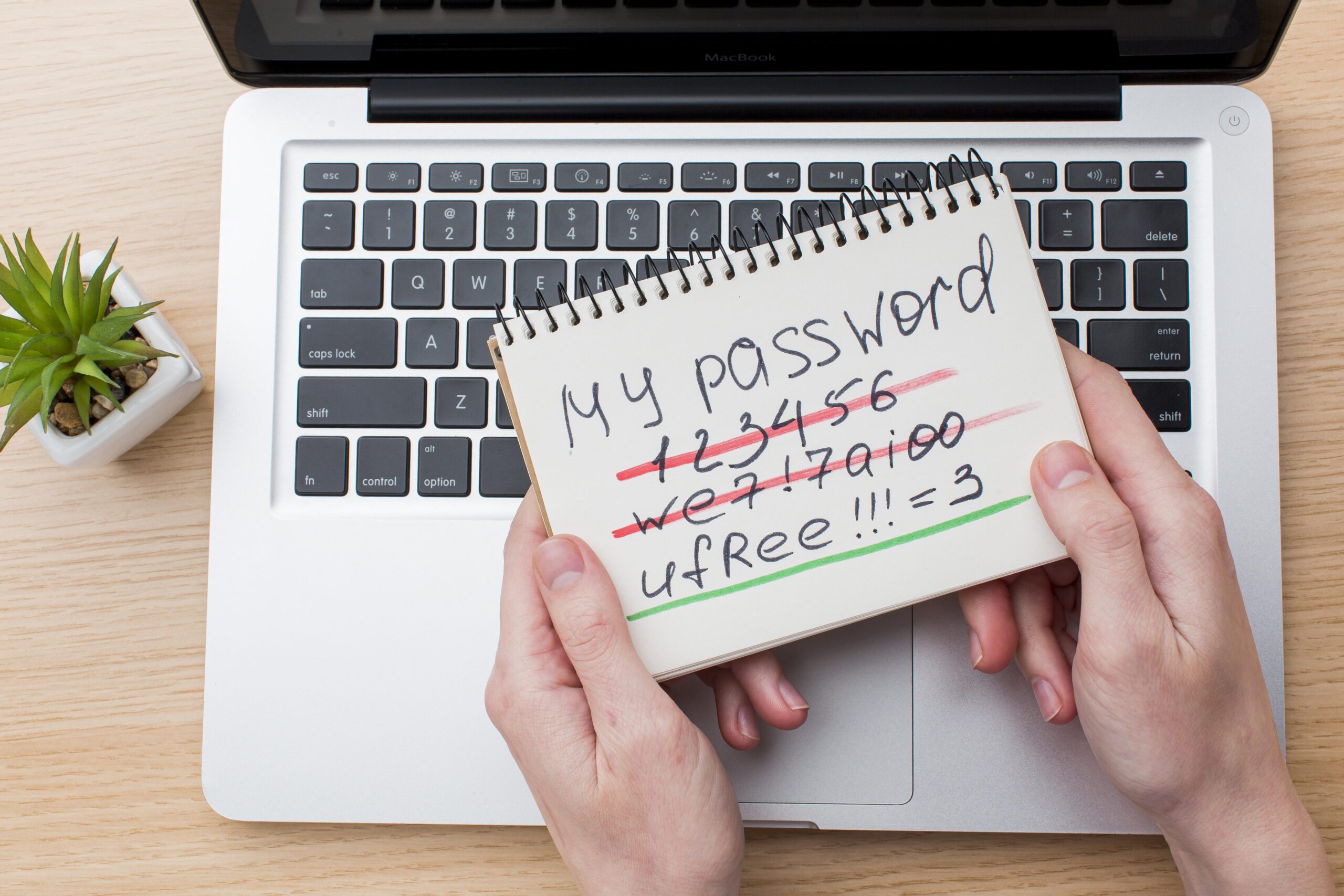 An employee holds a notebook with examples of weak and strong passwords over a laptop, highlighting the importance of secure password practices in cybersecurity training.